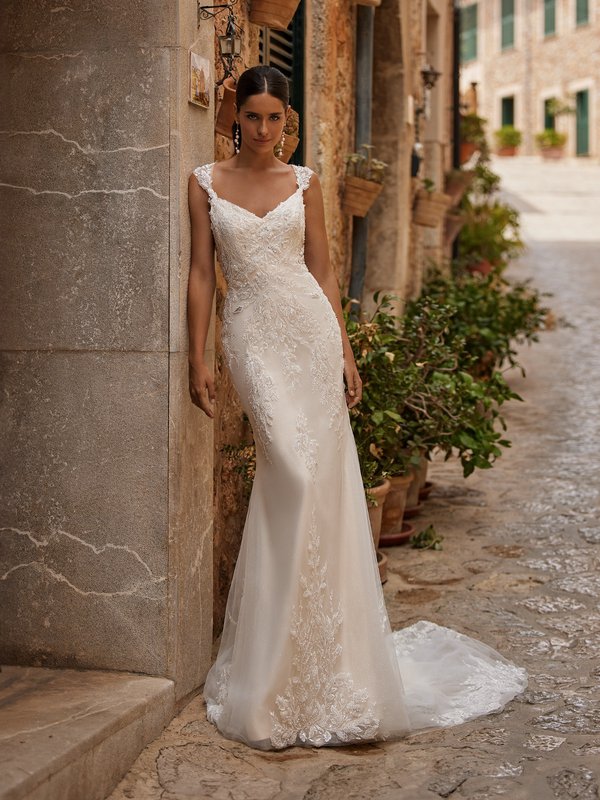 Bride leaning on wall while wearing fitted wedding dress with cap sleeves